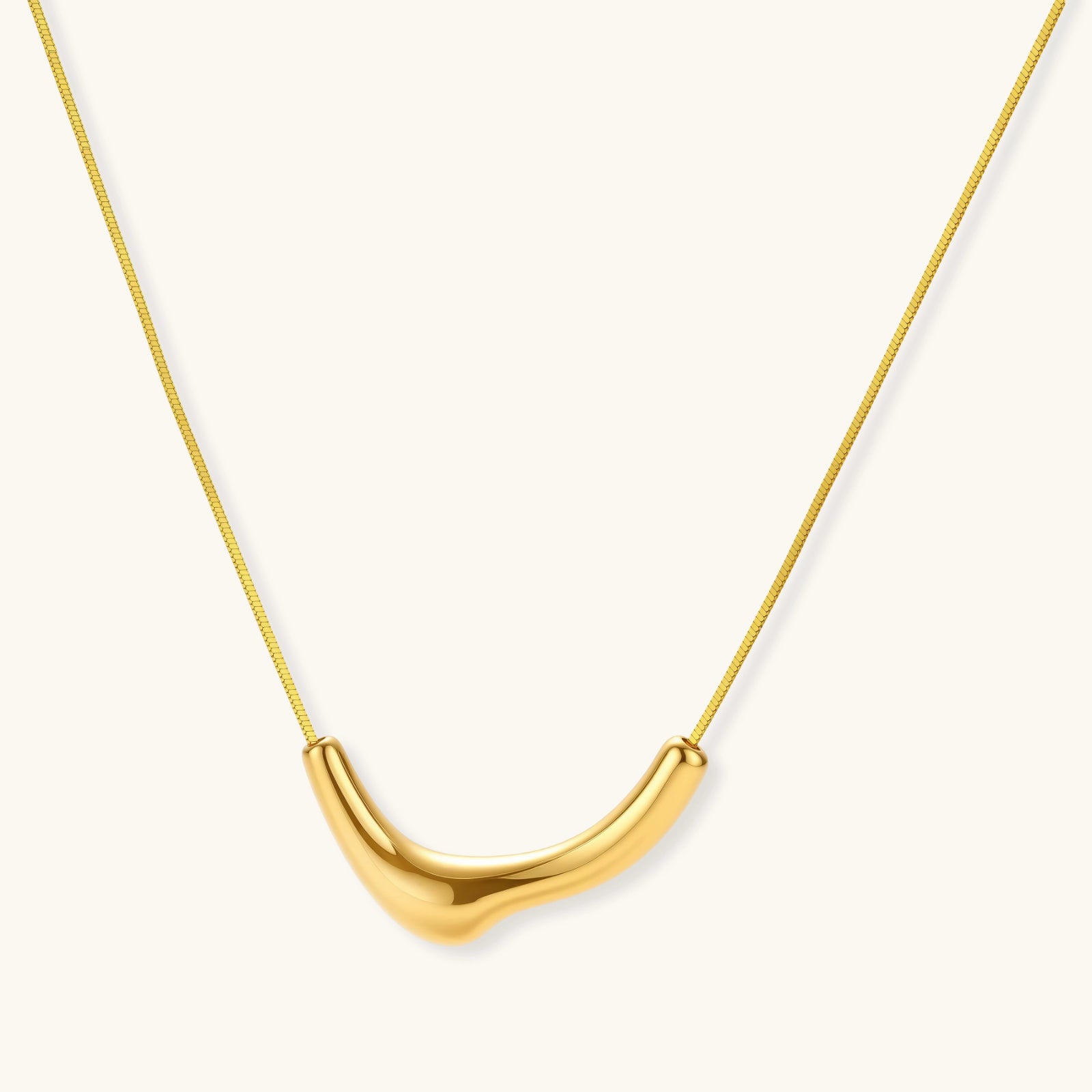 Minimalist gold-plated curved pendant necklace on delicate chain against cream background, showing adjustable length